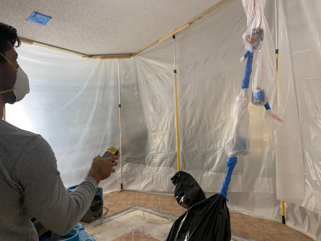 Technician in a respirator taking a moisture reading inside containment